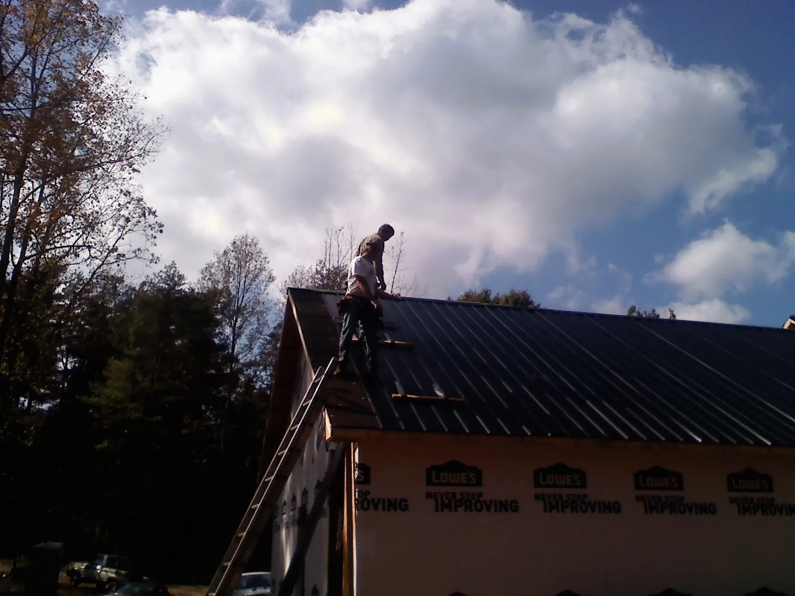 Roofer fastening dark metal panels high against a cloudy sky, from a Roof Inspection job in Lexington